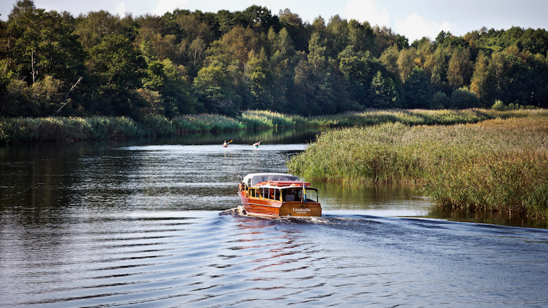 Båtbuss som åker på vattnet med mycket grön natur i bakgrunden