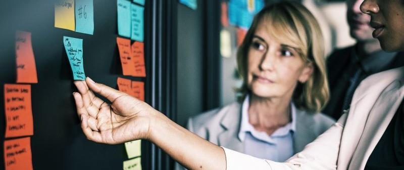 Tre personer sätter post-it lappar på en tavla.