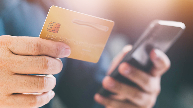 person håller ett betalkort och en mobil i handen