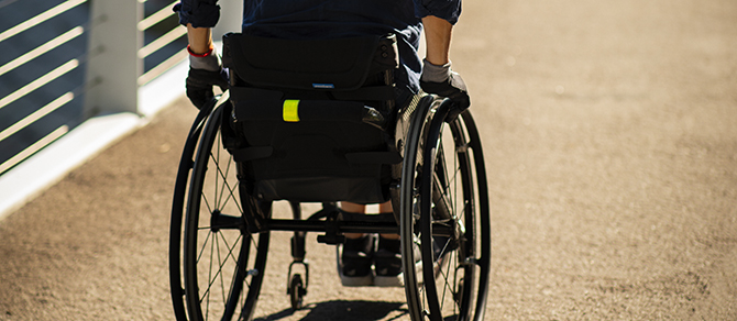 En kvinna i rullstol rullar uppför en bro 