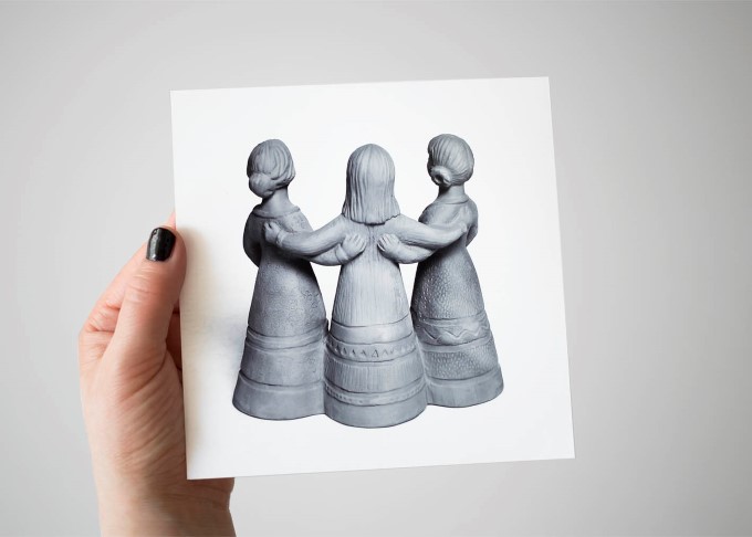 Någon håller upp ett svartvitt foto av terracottaskulpturen Tre trallande jäntor.