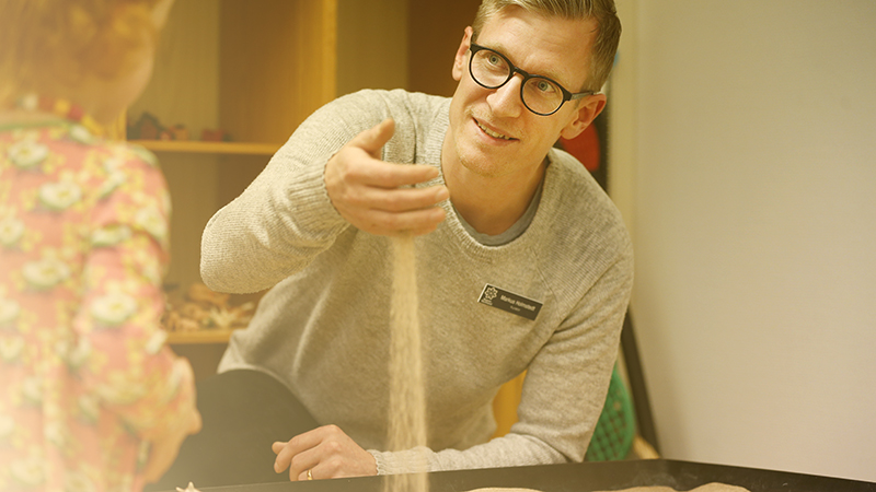 Man tittar på ett barn och silar sand mellan fingrarna. 