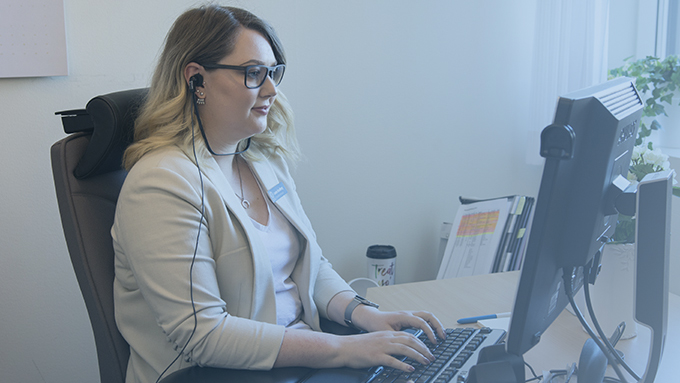 Kvinnas sitter och skriver framför en datorskärm.