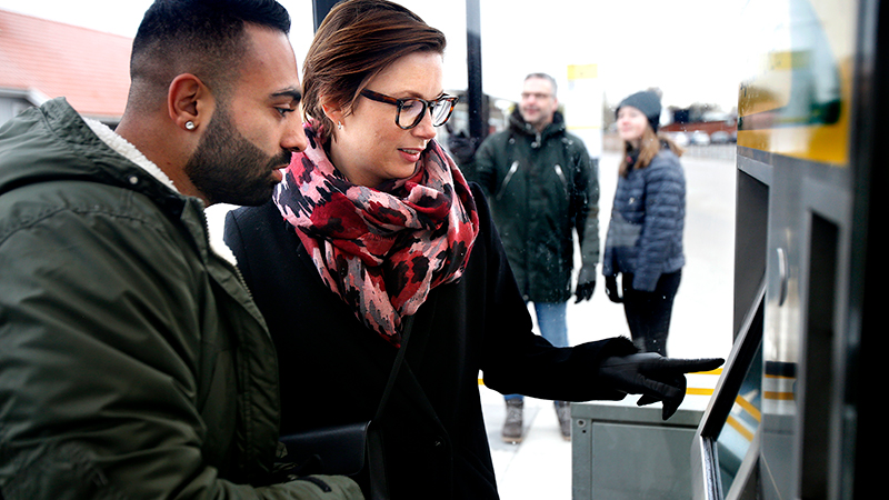 Två personer som använder en av Värmlandstrafiks biljettautomater.