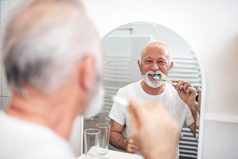 man borstar tänderna vid badrumsspegel