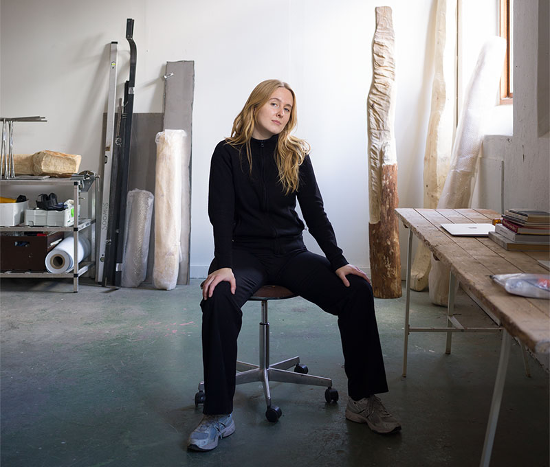 Kvinna klädd i svart sitter på pall i atlejé.