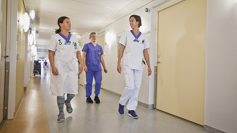Tre vårdklädda personer i en korridor.