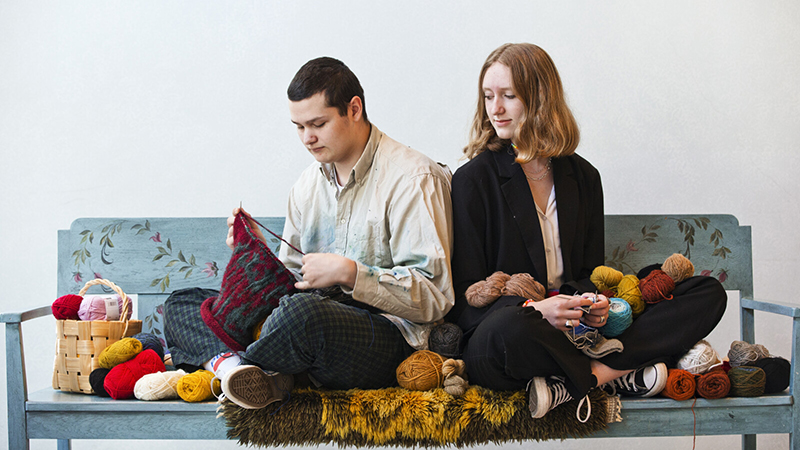 Två personer stickar i en soffa med massa garn.