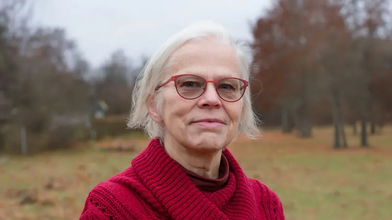 Gråhårig kvinna med röda glasögon och röd kofta.