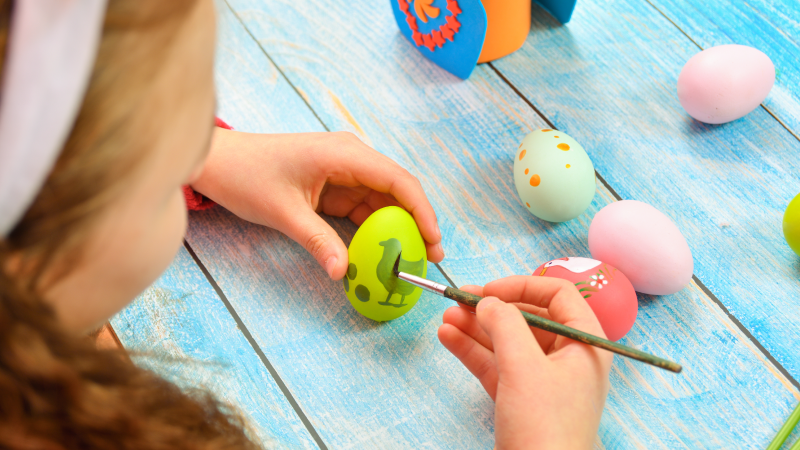 En tjej som sitter och målar ett påskägg.