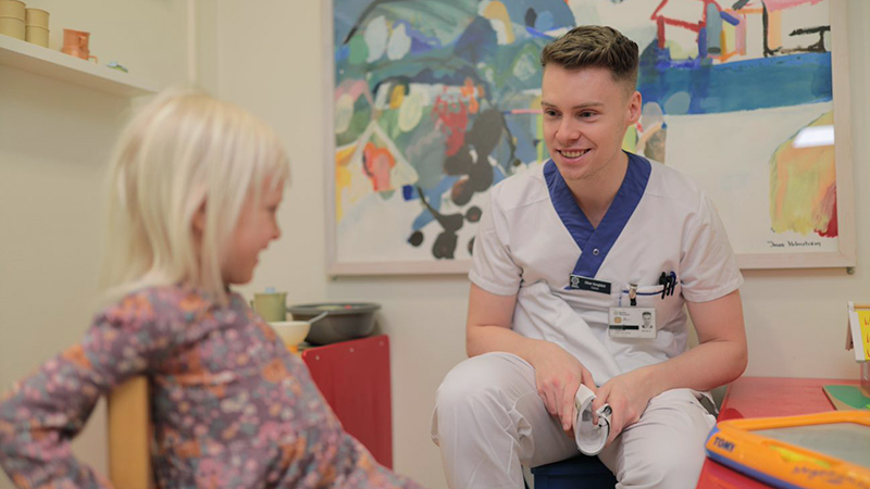 Ett barn och en man i arbetskläder sitter på barnstolar och ler mot varandra.