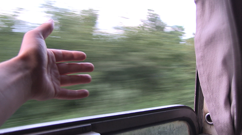 En hand sträcks ut genom öppet fönster på ett tåg på väg.