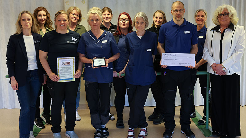 Medarbetare i blåa arbetskläder visar upp ett diplom och en prischeck.