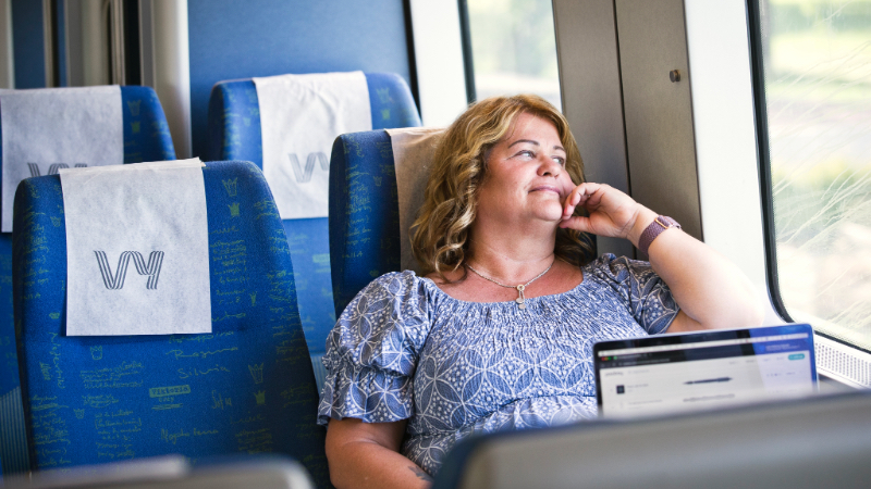 En kvinna sitter på ett tåg och kollar ut genom fönstret.