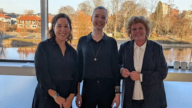 Porträtt på tre svartklädda kvinnor med en älv bakom.