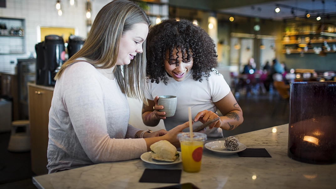 Två unga tjejer fikar på café.