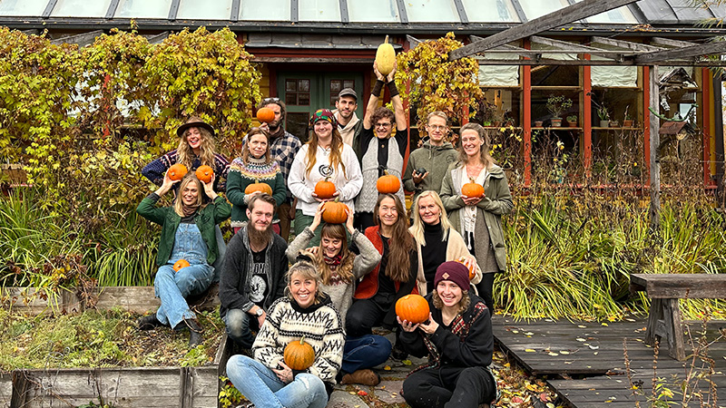 En gruppbild med människor som håller i pumpor framför ett växthus. 