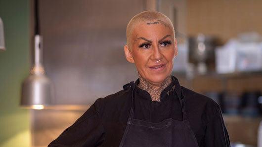 Kvinna med kortklippt hår i restaurangköksmiljö.