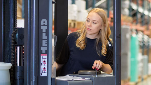 Ung kvinna kör truck på lager.