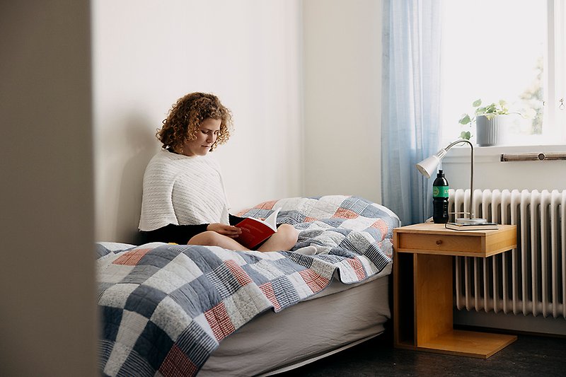 Ung person sitter i säng och läser bok
