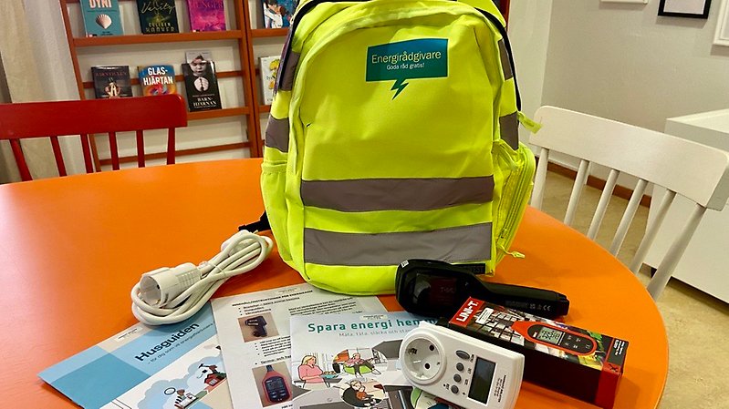 En gul ryggsäck. Framför den ligger bland annat broschyrer, elsladd och värmekamera.
