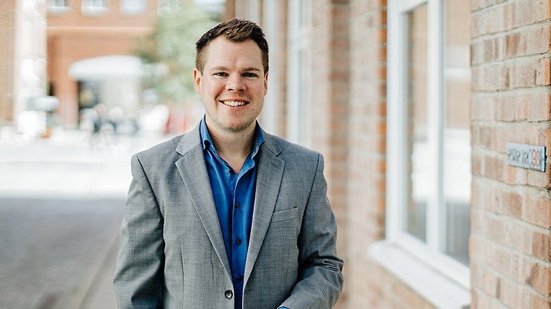 En man med grå kavaj tittar in i kameran och ler.